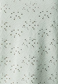 Tejido verde claro con intrincados bordados florales y recortes, creando un patrón y textura delicados en toda la superficie.
