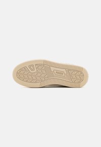 Semelle de sneaker beige avec un motif de grip texturé, comprenant un logo rectangulaire central et des rainures latérales pour une meilleure traction.