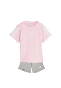 Camiseta de manga corta de color rosa claro con rayas blancas en los hombros y logo; combinada con pantalones cortos deportivos grises con un logo en el dobladillo.