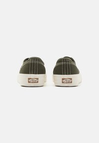 Zapatillas de lona verdes con costuras blancas, punta redondeada y suela de goma en color crema. Logo visible en el talón. Diseño sencillo y bajo.