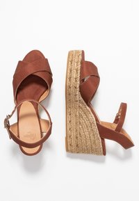 Hnědé kordurové sandály na klínu s křížovými popruhy, juteovým obloženým podpatkem a nastavitelným kotníkovým popruhem s kovovou přezkou.