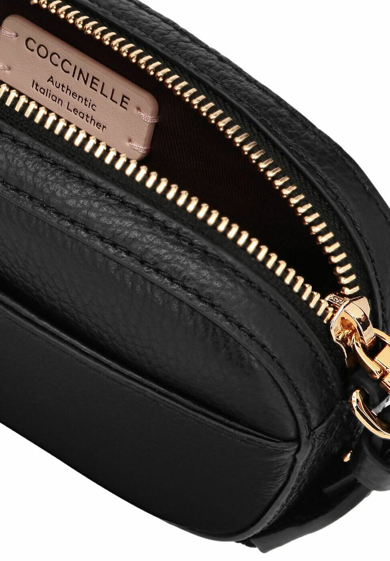 Schwarze Leder-Crossbody-Tasche mit goldfarbenem Reißverschluss und Beschlägen, strukturiertem Finish und beschriftetem Innenraum. Kompaktes und elegantes Design.