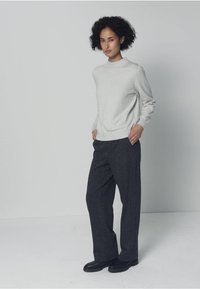 Vaaleanharmaa neulepaita korkealla kaula-aukolla, yhdistetty tummanharmaisiin leveälahkeisiin housuihin. Yksinkertainen malli, pehmeä rakenne, vähäiset koristelut.