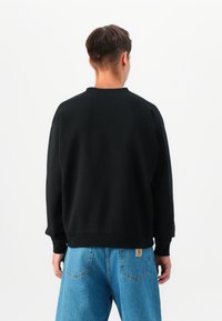 Črn pulover z okroglim izrezom, dolgimi rokavi in rebrastimi manšetami, v kombinaciji s svetlo modrimi denim hlačami z zadnjimi žepi.