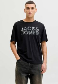 Sort kortærmet t-shirt med stort grafisk tryk "JACK & JONES" med et tekstureret design, stylet med mørkegrå jeans.