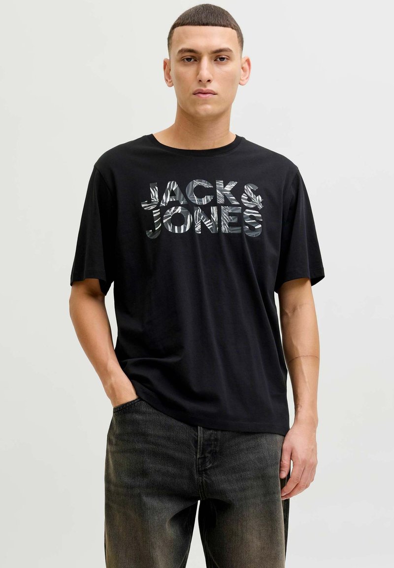 Sort kortærmet t-shirt med stort grafisk tryk "JACK & JONES" med et tekstureret design, stylet med mørkegrå jeans.
