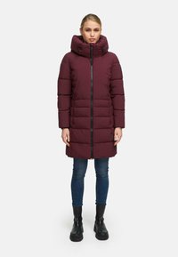 Bordeaux puffer jacket met een hoge kraag, ritssluiting en elastische accenten. Beschikt over een doorgestikt ontwerp en is gecombineerd met donkere spijkerbroeken en laarzen.