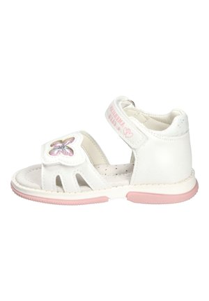 Biała sandałka dla małego dziecka z różową podeszwą, ozdobą w kształcie motyla na przednim pasku oraz regulowanym paskiem na kostkę z różowym napisem.