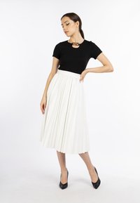 Zwarte korte mouwen top met een kettingaccent, gecombineerd met een witte geplooide midi-rok. Model draagt zwarte puntige hakken. Schone achtergrond.