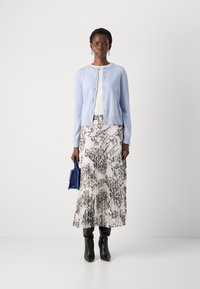 Lichtblauwe, gebreide cardigan met knopen over een wit topje, gecombineerd met een zwart-wit geprint plissérok en zwarte laarzen tot de knie.