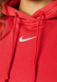 Rode hoodie van zachte stof, met een trekkoordkap en een wit Nike-logo op de voorkant. Fijne textuur, casual ontwerp.
