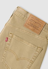 Τσέπη μπεζ τζιν Levi's που εμφανίζει την κόκκινη ετικέτα Levi's και δερμάτινο σήμα με τις λεπτομέρειες μεγέθους W32 L32 και Lot 511.