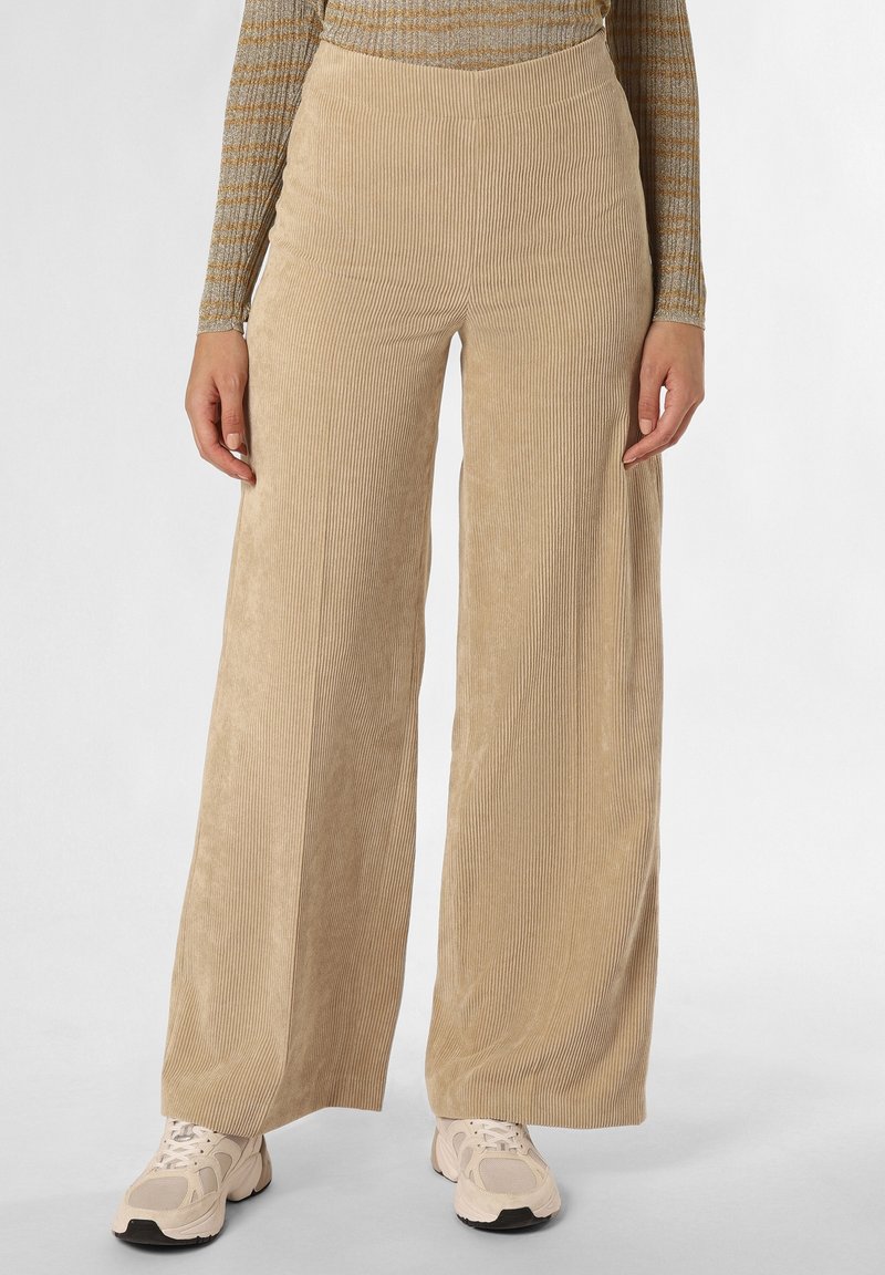 Pantalon large en velours côtelé beige porté avec des baskets beige et blanches et un haut à manches longues rayé, vu de la taille aux pieds.