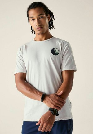 Man with braided hair wearing a white t-shirt with climbing logo, dark blue pants, a wristwatch, and a fitness tracker on left wrist.