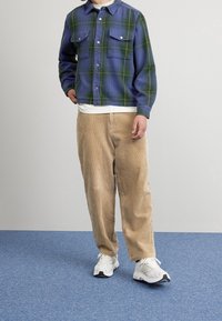 Rutiga flanellskjortor i blå och gröna nyanser med två bröstfickor; matchas med beige kordbyxor och vita sportskor.