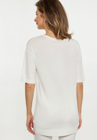 Hvid strikket top med korte ærmer, rund halsudskæring og en afslappet pasform. Blød tekstur med sideskår ved sømmen. Minimalistisk design.