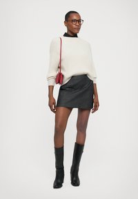 Jersey de punto color beige claro, minifalda de mezclilla negra, botas altas negras y un pequeño bolso rojo cruzado. Diseño simple y moderno con líneas limpias.
