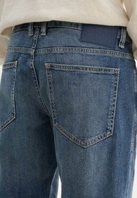 Denimjeans i medelblått med en slät textur, som har två bakfickor, diskret sömnad och en märkesläderlapp på midjan.