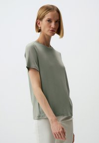 T-shirt verde chiaro a maniche corte in un tessuto morbido e liscio, con scollatura rotonda e vestibilità rilassata. Design minimalista, senza motivi o dettagli.