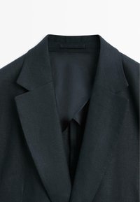 Tmavě šedé sako na míru s klopami se zářezem a viditelnou černou vnitřní podšívkou, zobrazené z horní přední části.