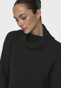 Pull en tricot couleur anthracite foncé avec un col roulé épais. Présente des motifs en losange texturés et des accents côtelés autour du col.
