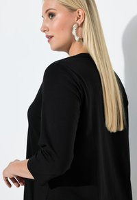Black, long-sleeve top with a smooth texture. Hair is long and straight, and there's a large, round, light-colored earring.