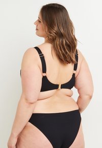 Set di bikini nero con spalline regolabili, hardware dorato, texture a coste e taglio classico. La vista dal retro mette in evidenza le spalline larghe e la chiusura.