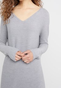 Pull en laine gris avec décolleté en V, manches longues et poignets sans doigts, présentant un tissu texturé pour le confort et une coupe décontractée.