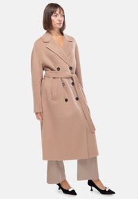 Trench coat in misto lana beige con design doppiopetto, ampi rever e vita cintrata, caratterizzato da bottoni neri e maniche lunghe.
