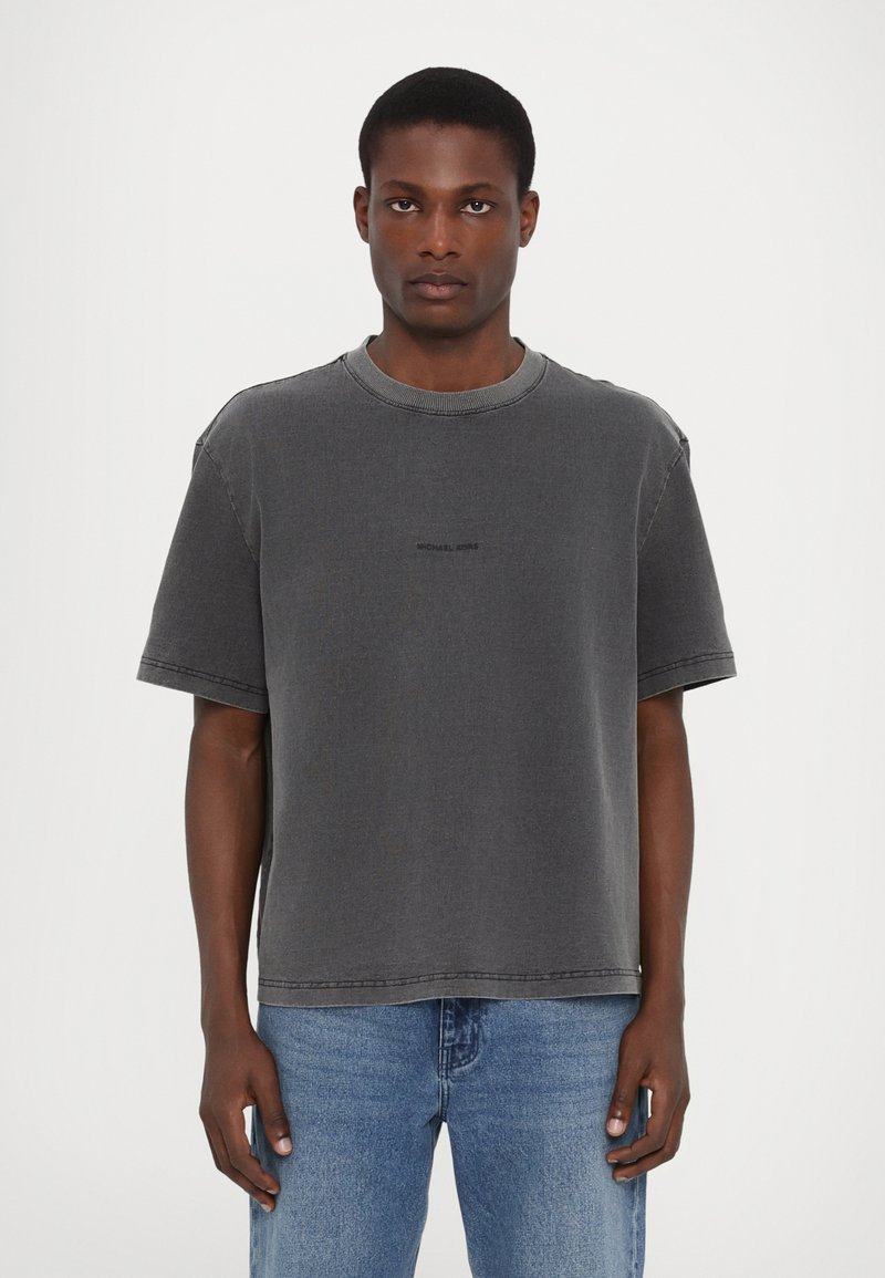 Grå bomulds T-shirt med rund hals, korte ærmer og sort logo på forsiden. Løs pasform med synlige syninger.