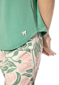 Een groene top met korte mouwen, versierd met een kleine roze strik aan de onderrand, gecombineerd met bloemenpatroonbroeken in roze en groen.