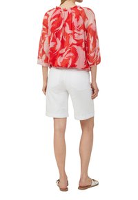 Blouse en chiffon à motifs rouges et roses avec des manches trois quarts, associée à un short en denim blanc. Des sandales blanches complètent la tenue.