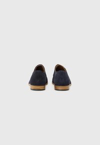 Chaussures en daim navy avec une silhouette basse et des semelles en bois brun ; elles présentent une texture lisse et un design simple sans embellissements.