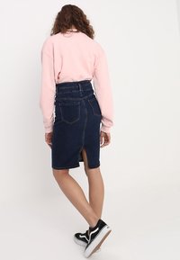 Mörk denimkjol med hög midja, slits bak och två bakfickor. Kombinerad med en rosa sweatshirt och svarta sneakers.
