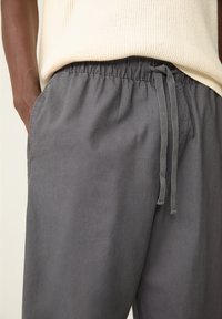 Graue, leichte Baumwollhosen mit elastischem Taillenzug, verstellbarem Kordelzug und Seitentaschen, die eine entspannte Passform und eine glatte Textur bieten.