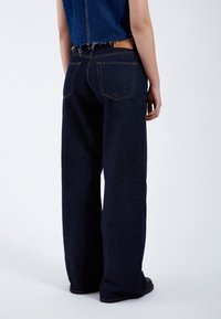 Vaqueros acampanados de denim azul oscuro, con cintura alta, dos bolsillos traseros y costuras de contraste. Con un ajuste relajado.