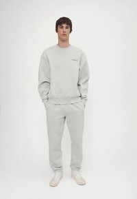 Gaiši pelēks džemperis un tam atbilstošas sporta bikses, kokvilnas maisījums, brīva piegriezuma, ar ribām aprocēs, minimālistisks dizains, baltas sporta kurpes, izšūta logo.