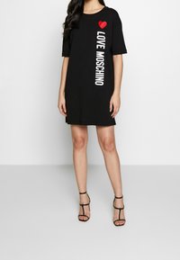 Svart t-shirtklänning med ett rött hjärta och "LOVE MOSCHINO" i vit text. Korta ärmar och lös passform, tillverkad av mjukt bomullsmaterial.