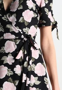 Schwarzes Wickelkleid mit rosa Rosenmuster, ausgestattet mit kurzen Ärmeln mit Bindebändern, einem gebundenen Taillen-Detail und einer fließenden Silhouette. Glatter Stofftextur.