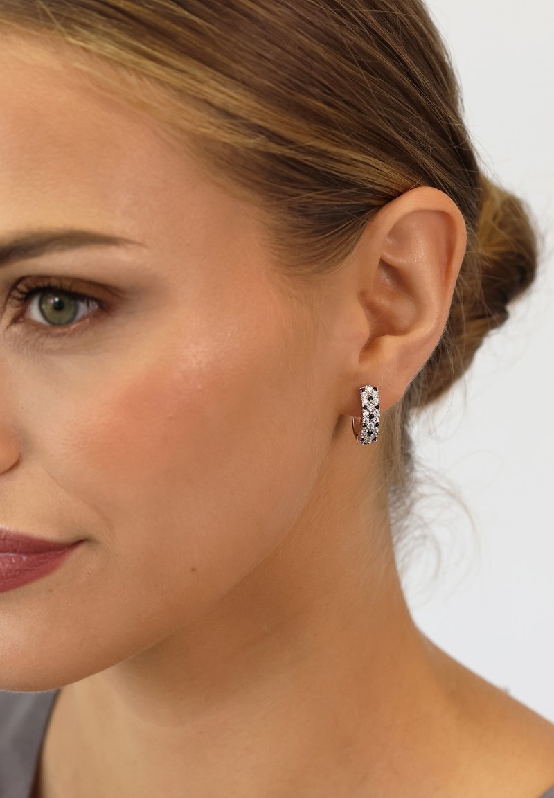 Silver hoop earrings featuring a textured surface with black and white patterns, set against a neutral backdrop for contrast.