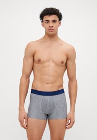 Sivi bokserice s plavim elastičnim pojasom na kojem piše "UNDER ARMOUR" u podebljanim slovima. Tkanina izgleda mekano i s teksturom.