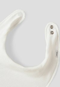 Hvid ribbet babyserviet med en buet form, der har trykknaplukninger ved halsen og en blød, struktureret overflade. Mærket etikette synlig.