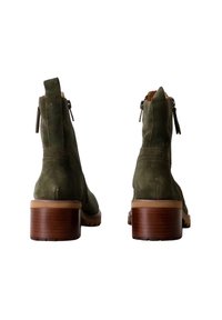 Stivaletti alla caviglia verde in suede con zip laterale, tacco a blocco e suola texturizzata color tan. Presentano un design minimalista e linee pulite.