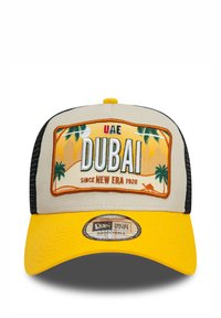 Gorra de camionero con parte delantera beige, visera amarilla y parte trasera de malla negra. El parche frontal muestra "DUBAI" con gráficos de palmeras y un horizonte desértico.
