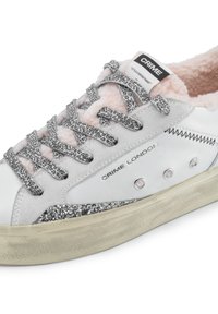 Sneaker bianca con fodera in pelliccia sintetica rosa, lacci con stampa leopardata e dettagli in glitter argento. Presenta marchi e cuciture decorative.