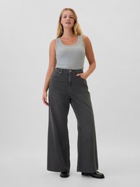 Débardeur gris associé à un jean gris à taille haute et jambes larges. Le pantalon présente une fermeture à bouton et des poches latérales, fabriqué en denim.