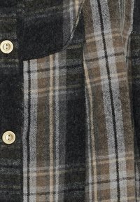 Flannelskjorte med tern i mørkegrå og beige toner. Har en brystlomme og lyse knapper. Blødt, tekstureret stof.