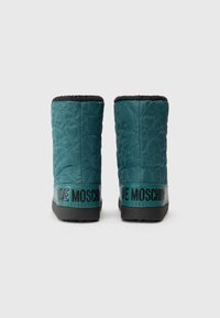 Turkizne zamešane gležnjače s črnim obrobom in teksturiranim vzorcem srca. Imajo črn gumijast podplat in blagovno znamko "LOVE MOSCHINO" na zadnji strani.