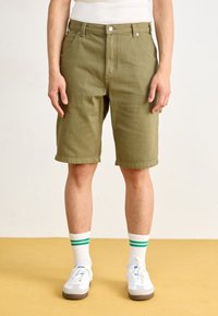 Olive green cotton shorts with a straight cut, featuring a flat front, belt loops, and cuffed hems, paired with white sneakers and socks.