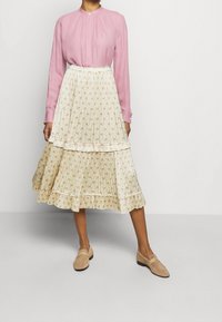 Rosa långärmad blus med knapplinkning, krämfärgad blommönstrad plisserad kjol med volanger, kombinerat med beigea slip-on skor.